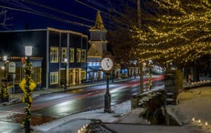 Easton, MA Main Street picture with holiday lights on buildings, posts and trees. Includes clock on street with light snow cover.